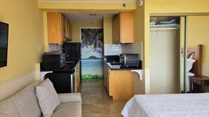 Ein kompaktes Hotelzimmer mit Küchenzeile, einer Couch, einem Bett und Blick auf einen tropischen Strand.