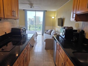 A modern kitchen with a large island, a dining area with a sofa, and a balcony with a city view. - 20th Fl Inn on the Park | Diamond Head & Ocean View | AC | Pool (Honolulu)