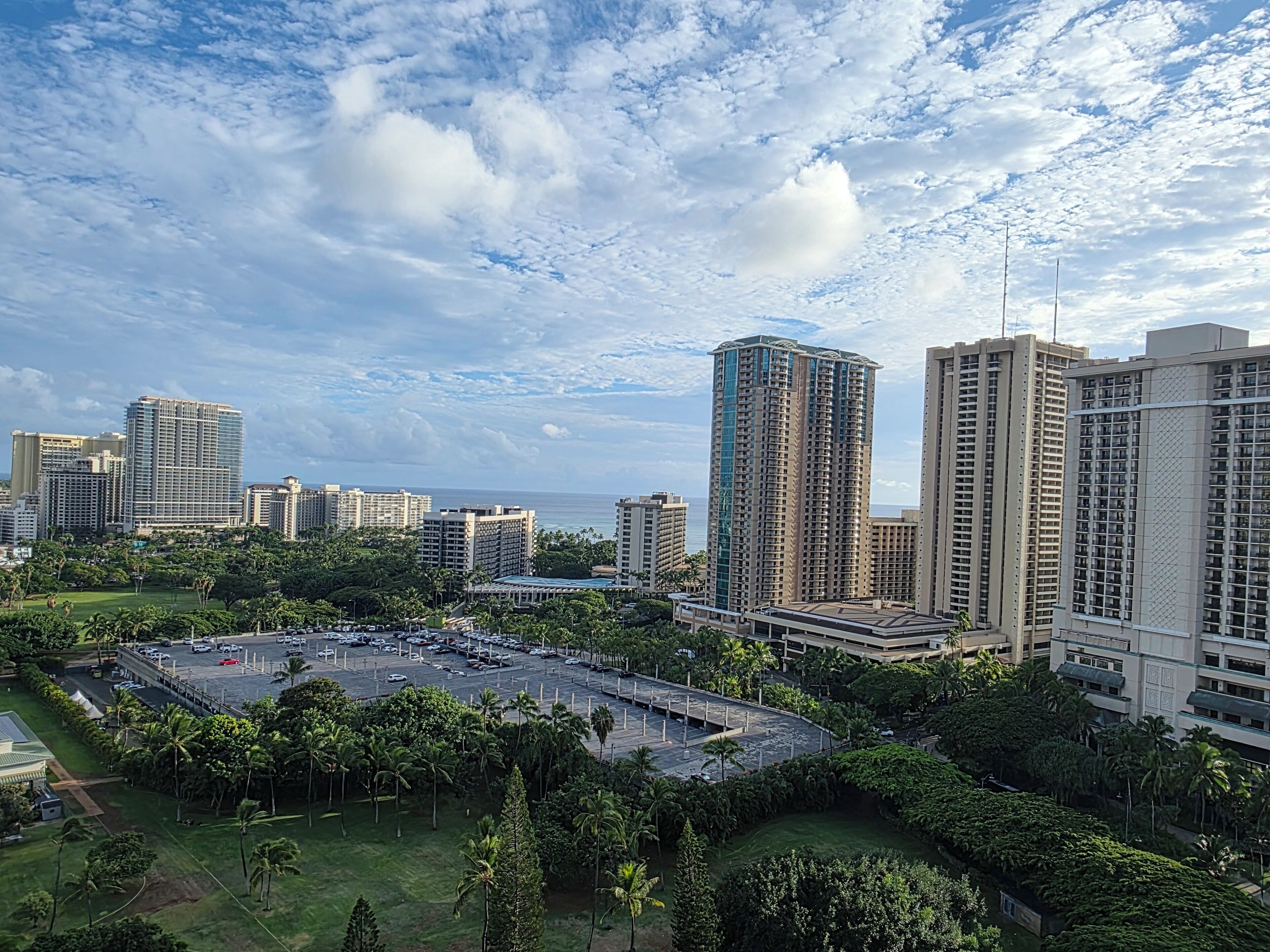 A high-rise hotel with multiple floors, a parking lot, and a view of the ocean.