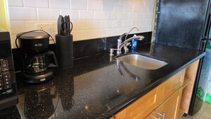 Eine Küche mit schwarzer Arbeitsplatte, einer Kaffeemaschine, einem Spülbecken und einem Kühlschrank.