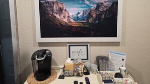 A coffee machine, a framed picture of a mountain landscape, a sign with wifi password, and a tray with coffee cups and a tissue box. - Bluebird Place (Elk City)