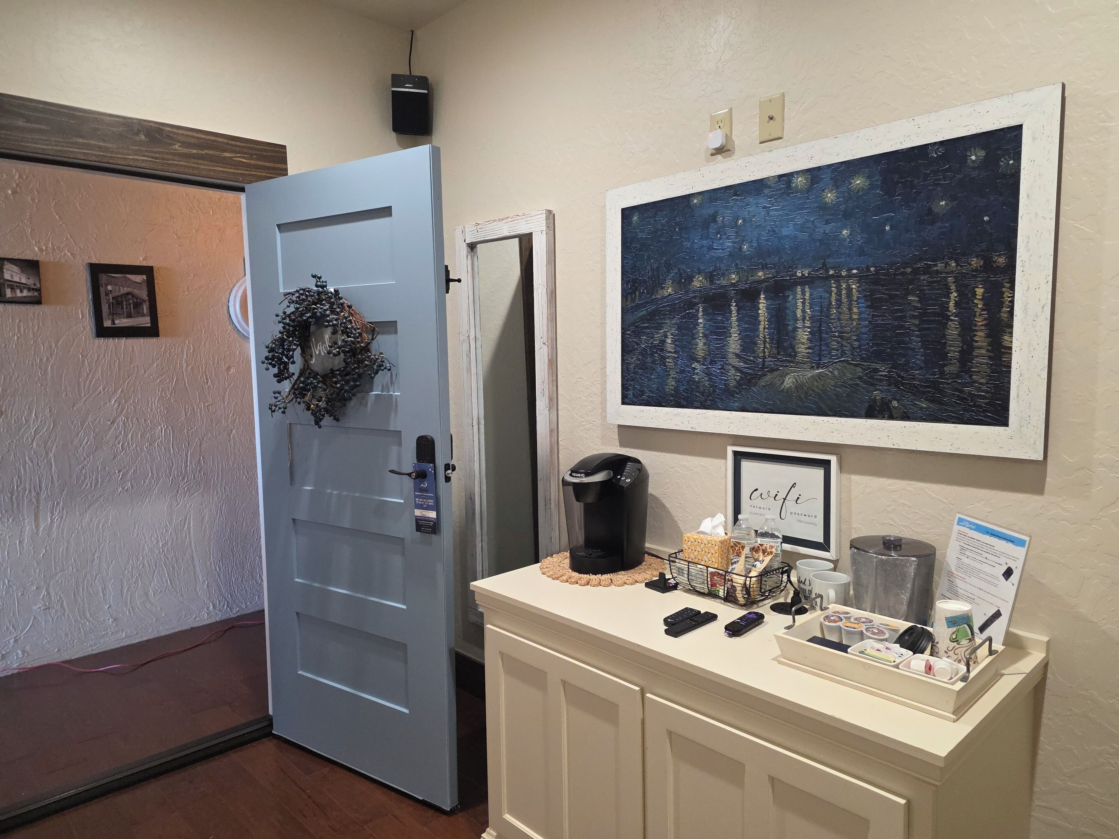 Un vestíbulo de hotel con una puerta, una máquina de café, una obra de arte enmarcada y una recepción con servicios.