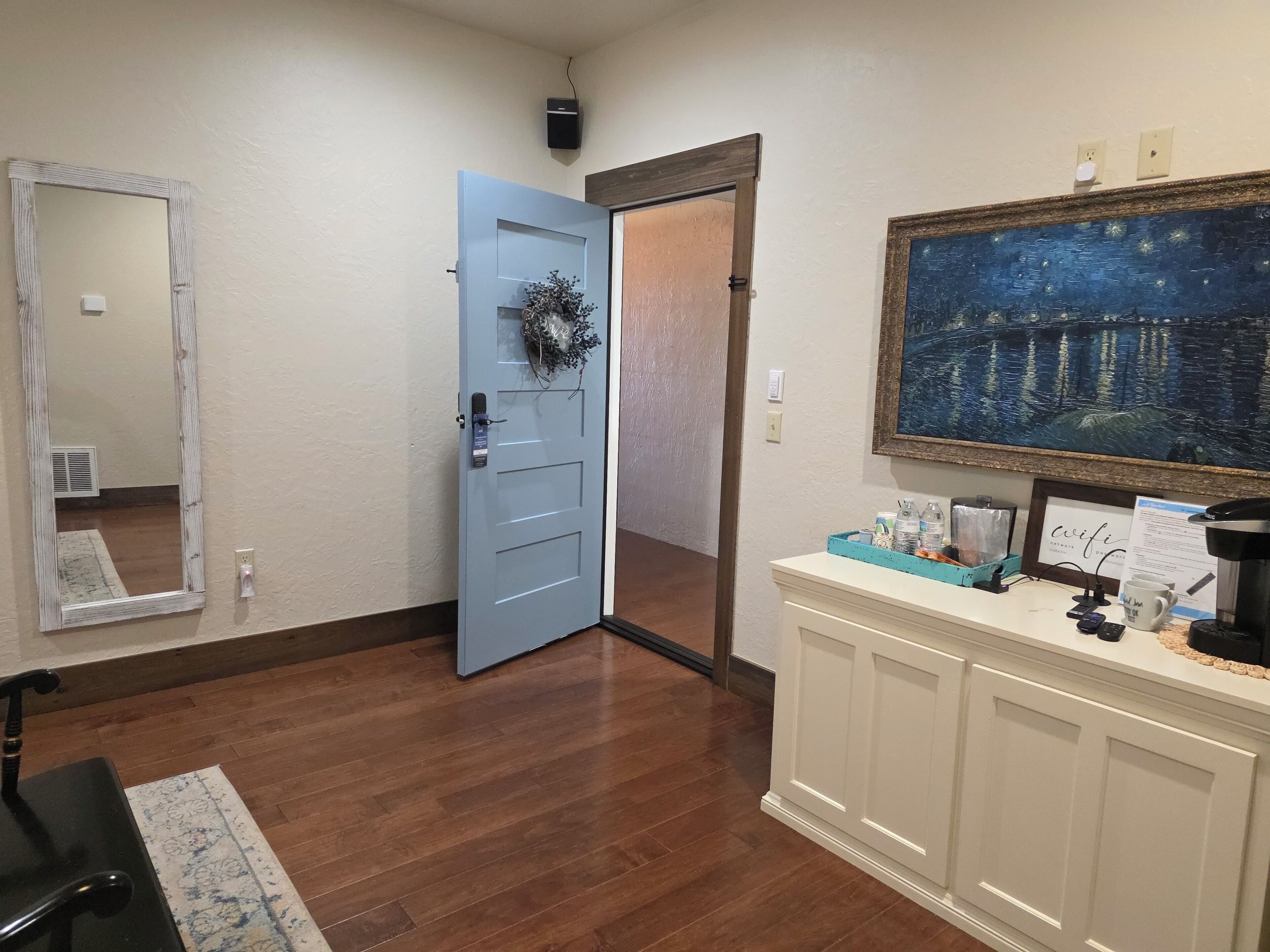 A hallway with a blue door, a mirror, a painting, and a white console table with various items.