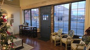A cozy room with a wooden floor, a Christmas tree, a dining table with chairs, and large windows with a view of the street. - Bluebird Place (Elk City)