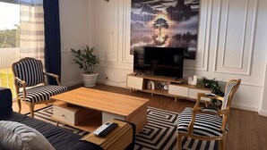 Ein modernes Wohnzimmer mit einem großen Flachbildfernseher, gestreiften Polstersesseln, einem Holztisch und einer Zimmerpflanze.