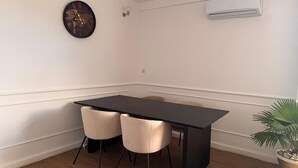 Ein Zimmer mit einem schwarzen Tisch, zwei Stühlen, einer Klimaanlage, einer Wanduhr und einer Topfpflanze.