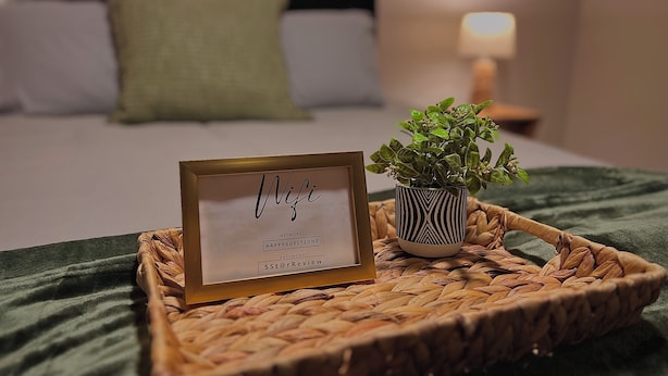 A bed with a green blanket, a small potted plant, and a framed sign with the word "Wifi" and network details.