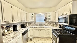 A compact kitchen with white cabinets, a gas stove, a microwave, and a sink.