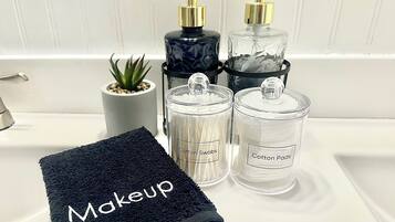 A bathroom sink with a black towel labeled "Makeup," two glass containers labeled "Cotton Swabs" and "Cotton Pads," and a small potted plant.