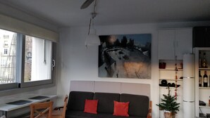 Ett vardagsrum med en soffa, ett litet bord, en krukväxt och en tavla på väggen.