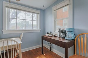 Una habitación con una mesa de madera, dos sillas, un ventanal y una cafetera.