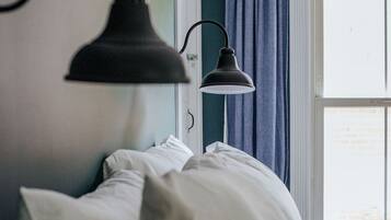 A bedroom with a bed, white pillows, a black wall-mounted lamp, and a window with blue curtains.