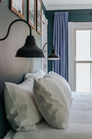A bedroom with a bed, white pillows, a black wall-mounted lamp, and a window with blue curtains.