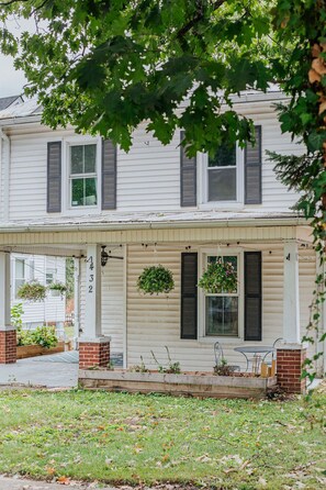 A two-story house with a covered porch, a brick foundation, and hanging flower baskets. - The Wayne Shire: Sleeps 8 + Downtown Waynesboro (Waynesboro)