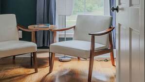 A room with two chairs, a table, a ceiling fan, a window with curtains, and a door.