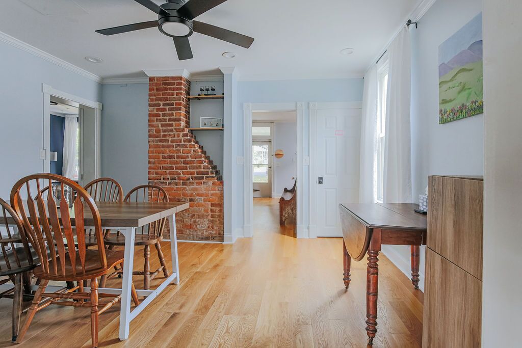 A dining area with a brick fireplace, wooden chairs, and a ceiling fan.