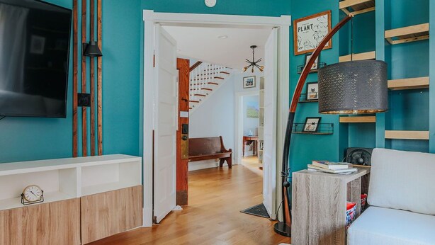 Un salon moderne aux murs de couleur turquoise, doté d’un parquet, d’un téléviseur fixé au mur et d’un escalier menant à une autre pièce.