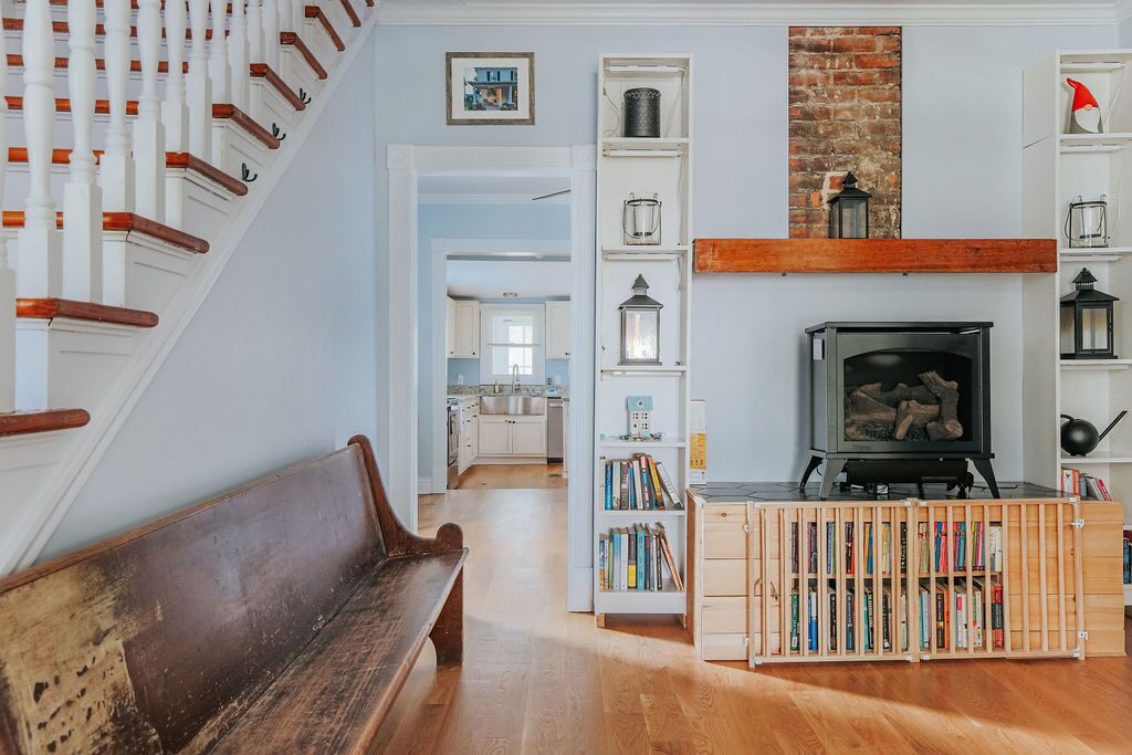 A staircase with white balusters and wooden handrails, a wooden bench, a fireplace with a black surround, and a bookshelf with various items.