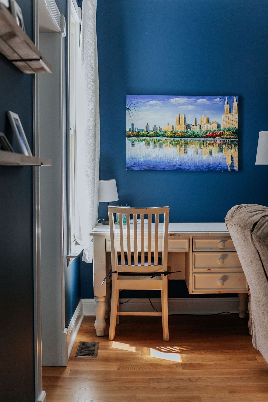 Une pièce comprenant un bureau, une chaise et un tableau représentant un paysage urbain accroché au mur.