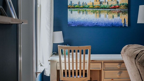 A room with a desk, chair, and a painting of a cityscape on the wall.