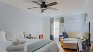 Une chambre d’hôtel comprenant un lit, un bureau, une chaise, un canapé, un ventilateur de plafond et une fenêtre avec des rideaux.