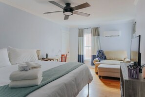 Ein Hotelzimmer mit einem Bett, einem Schreibtisch, einem Sessel, einer Couch, einem Deckenventilator und einem Fenster mit Vorhängen.