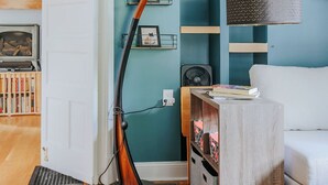 Une pièce aux murs de couleur turquoise, avec une porte blanche, un plancher en bois, un canapé blanc, une lampe, des étagères ornées d’objets décoratifs et un tableau encadré accroché au mur.