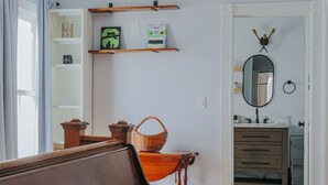Une pièce comprenant un banc en bois, un miroir, des étagères ornées d’objets décoratifs et une porte donnant sur une autre pièce.