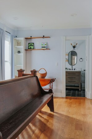 Ein Zimmer mit einer hölzernen Sitzbank, einem Spiegel, Regalen mit Dekoration und einer Tür zu einem weiteren Raum.