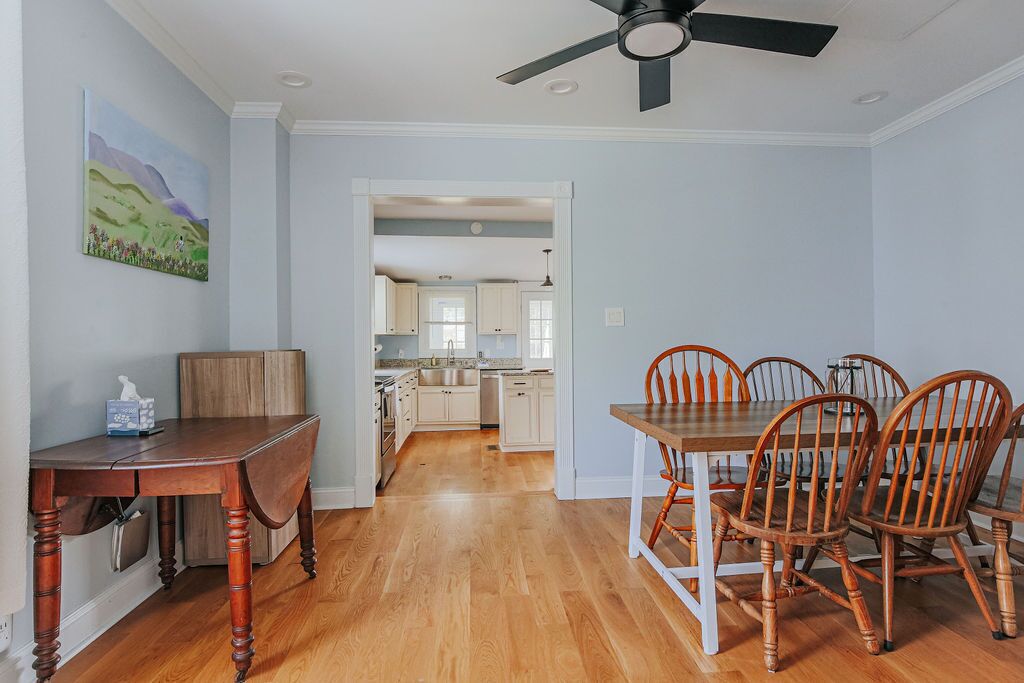 A dining area with a wooden table and chairs, a ceiling fan, and a view into the kitchen.