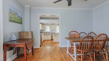A dining area with a wooden table and chairs, a ceiling fan, and a view into the kitchen.