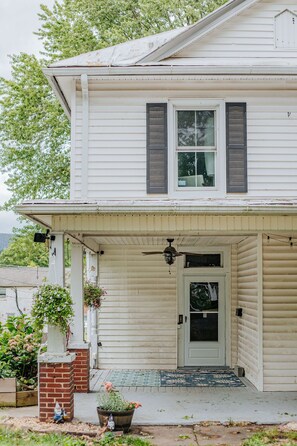 A two-story house with a front porch, a door with a glass panel, and a small garden area with potted plants. - The Wayne Shire: Sleeps 8 + Downtown Waynesboro (Waynesboro)