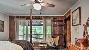 A bedroom with a bed, a wooden dresser, a chair, a ceiling fan, and a window with curtains. - Treetop Terrace Cottage (Interlochen)