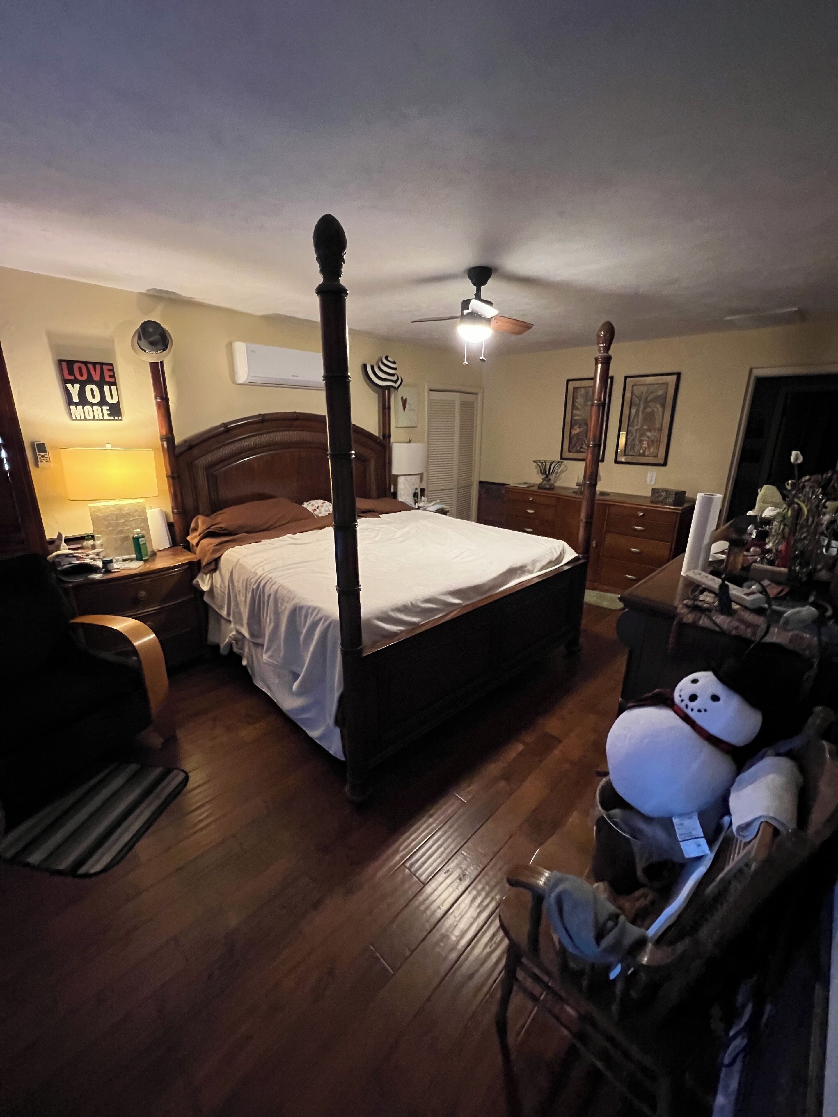 Een slaapkamer met een hemelbed, een plafondventilator en een nachtkastje met een lamp.