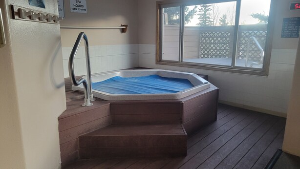 Ett spaområde med ett bubbelbad, trästeg, ett fönster och en skylt som anger spats öppettider.