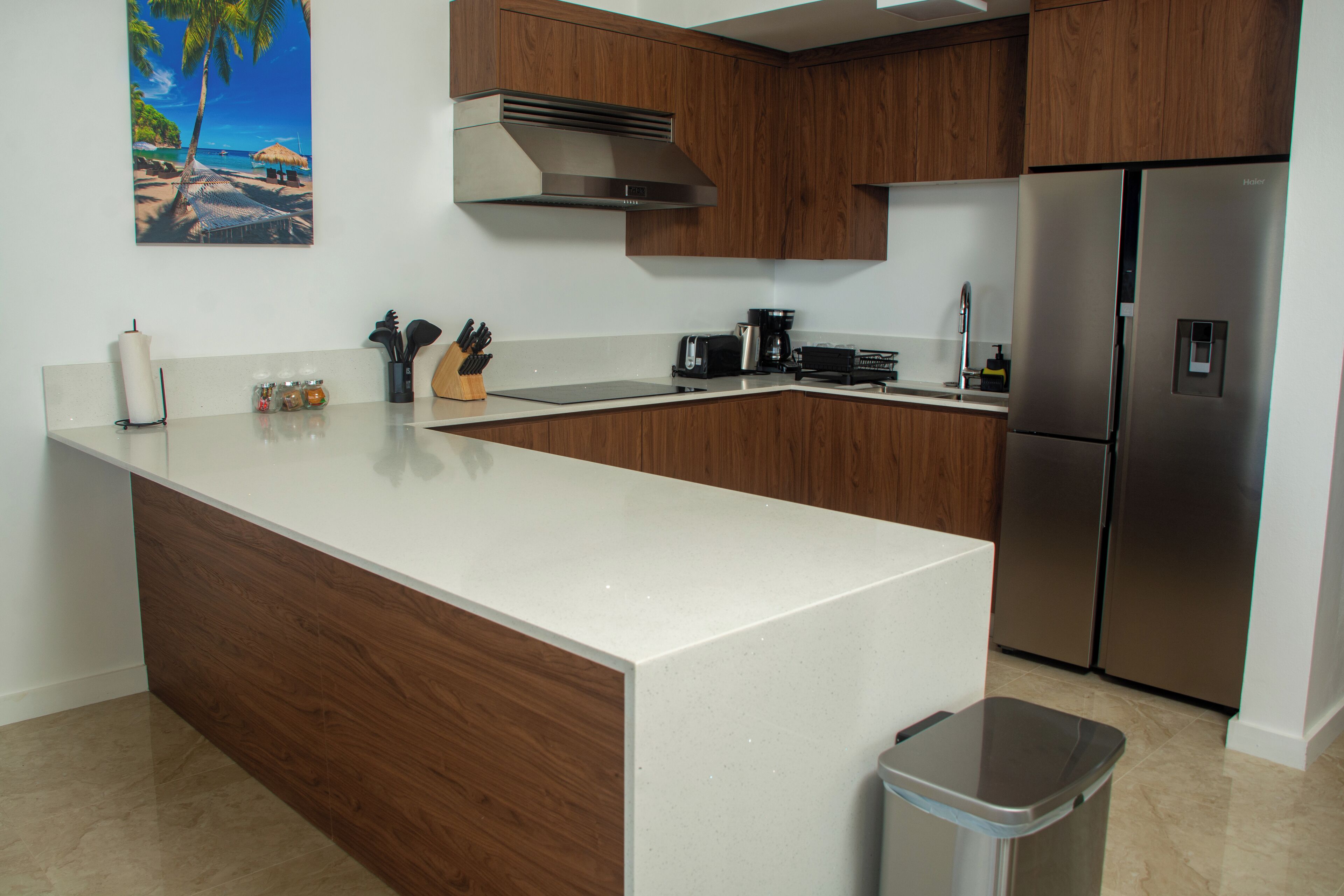 A modern kitchen with wooden cabinets, a stainless steel refrigerator, and a white countertop.
