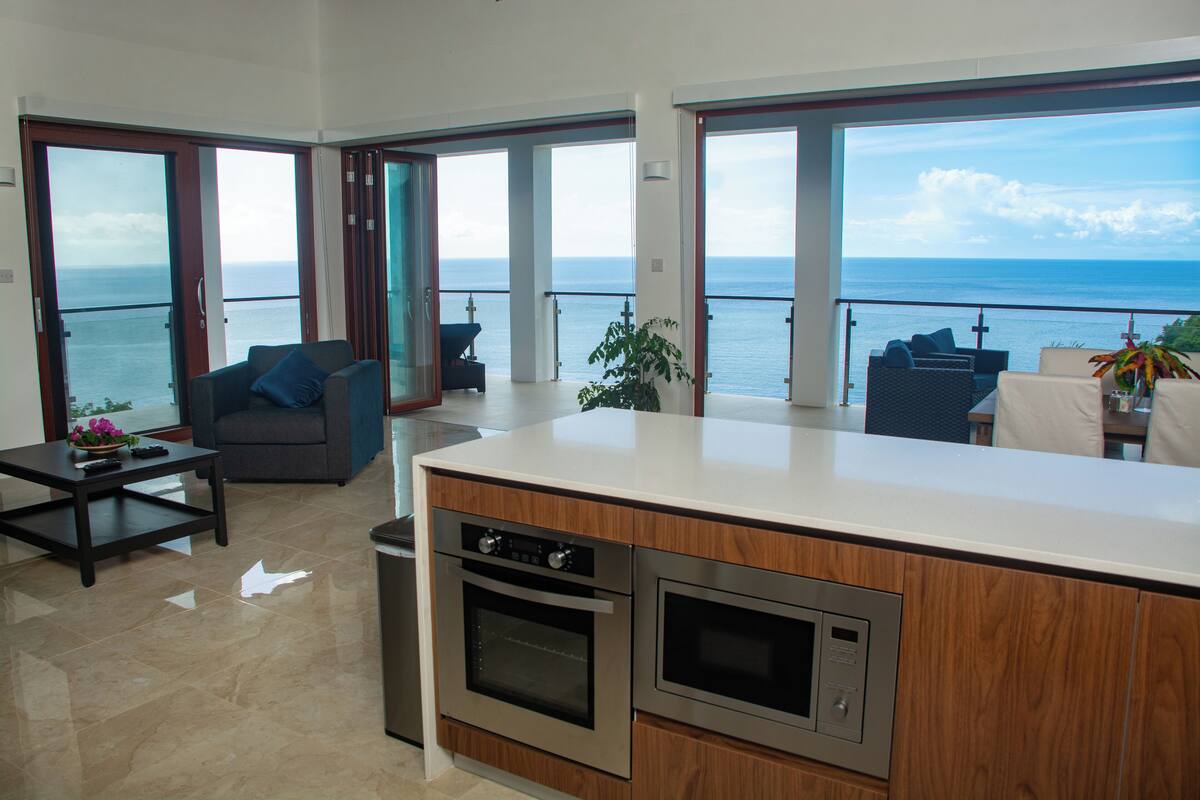 A modern kitchen with a large island, a dining area with a view of the sea, and a cozy seating area with a sofa and a coffee table.
