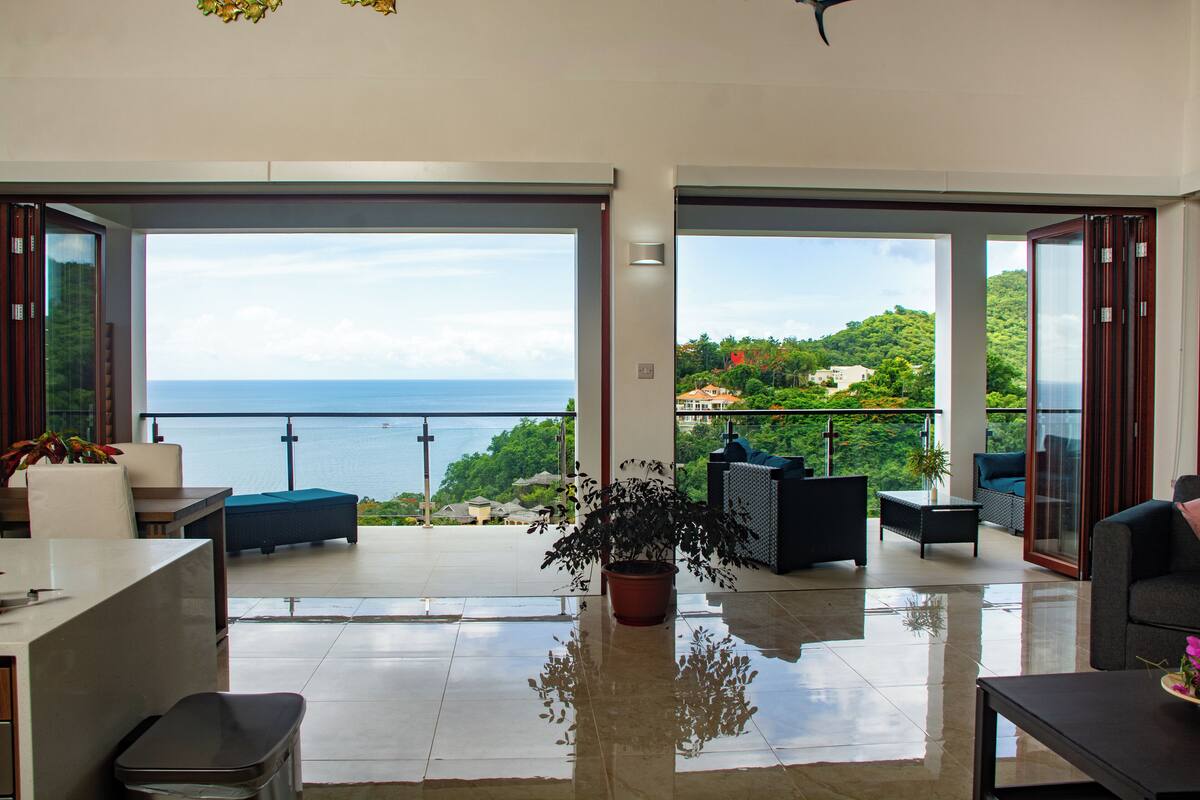 A spacious living area with a large sliding glass door leading to a balcony with a view of the sea.