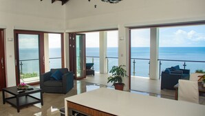A spacious living area with a large window overlooking the sea, a sofa, a coffee table, and a potted plant. - Villa Vino Lucia & Helen's Wine Cellar (Marigot Bay)