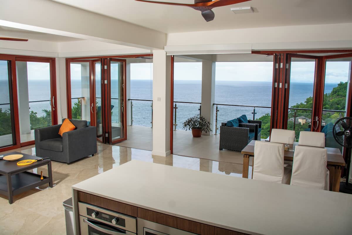 A spacious living area with a large view of the sea, a balcony with outdoor furniture, and a modern kitchen.