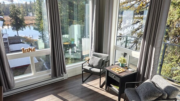 A modern room with large windows overlooking a lake, furnished with two chairs and a small table. - Turtle Loft Lakefront Cabin Townhome (Kootenay Boundary E / West Bo*)
