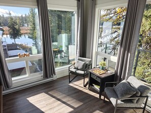 A modern room with large windows overlooking a lake, furnished with two chairs and a small table. - Turtle Loft Lakefront Cabin Townhome (Kootenay Boundary E / West Bo*)