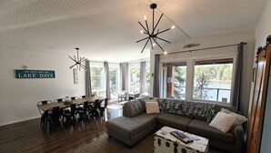 A spacious living room with a large sectional sofa, a dining table with chairs, and a unique white chest of drawers. - Turtle Loft Lakefront Cabin Townhome (Kootenay Boundary E / West Bo*)