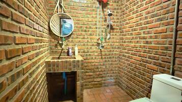 Een kleine, afgesloten badkamer met een bakstenen muur, een toilet, een wastafel met spiegel en een douchehoek.