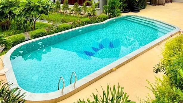 Ein Schwimmbad mit Holzterrasse und einem Haus mit Strohdach.