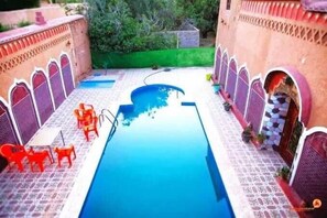 A pool area with a blue pool, red chairs, and a small table. - Kasbah Ifri (Souk Lakhmis Dades)