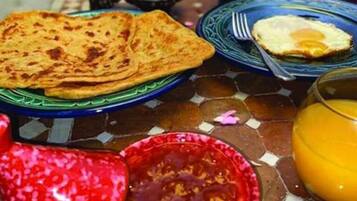 A breakfast table with a plate of flatbread, a fried egg, a glass of orange juice, and a bowl of tomato sauce.