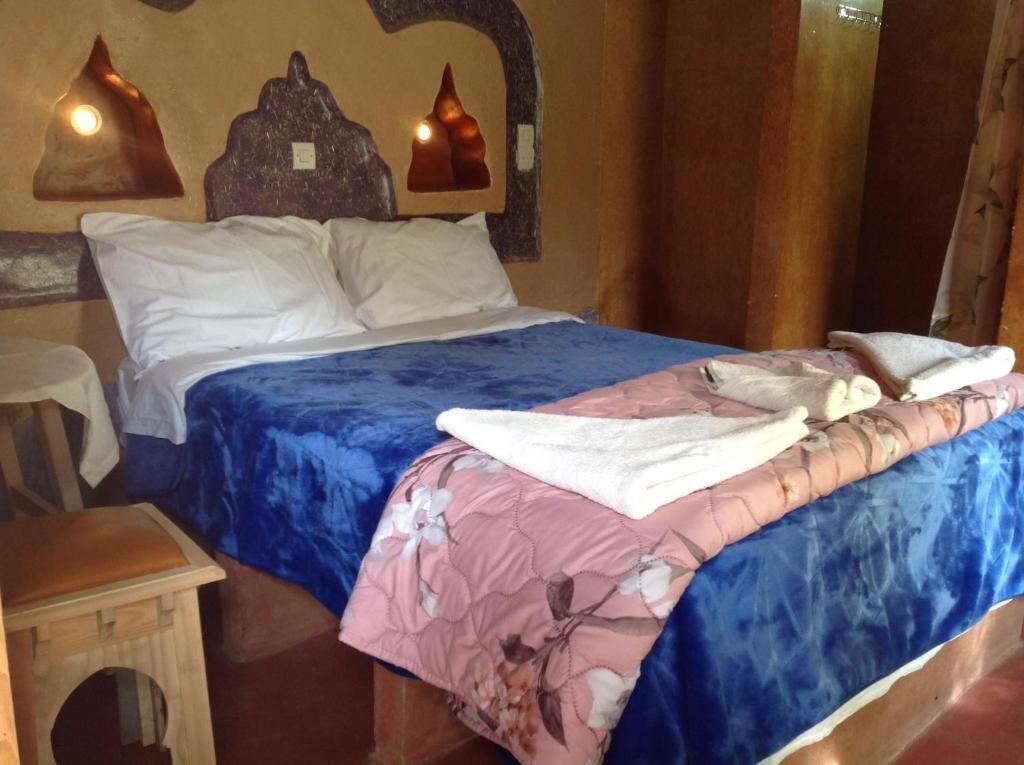 Een bed met een blauw-roze bloesemkleed, twee witte kussens en een houten nachtkastje.