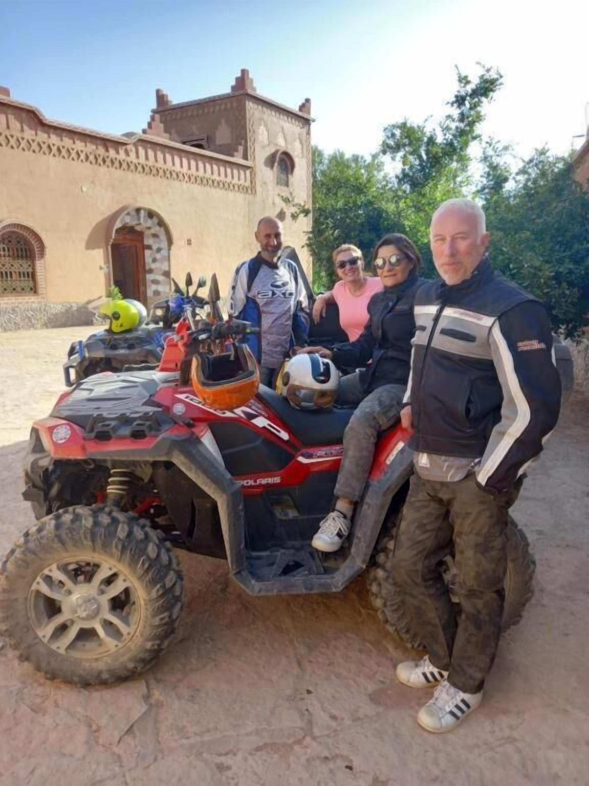 A group of people posing with a Polaris ATV in front of a building with arches and stone walls.