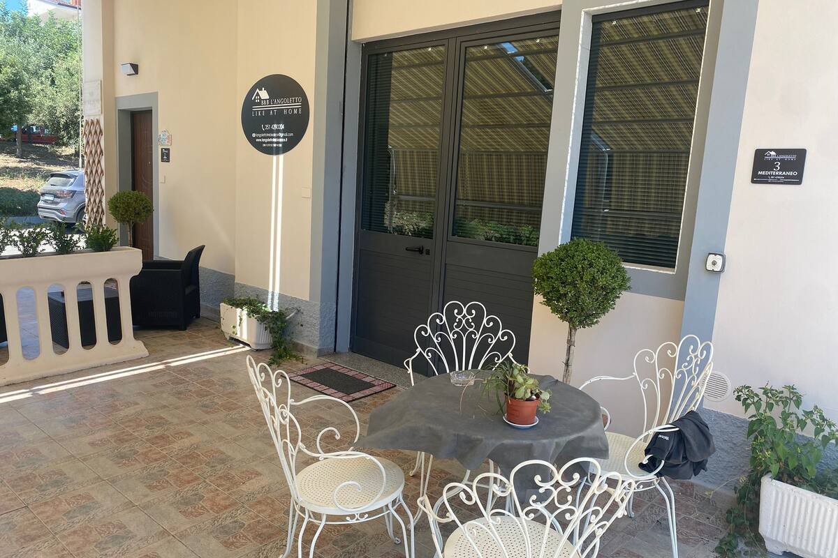 An outdoor seating area with a table and four chairs, a small potted plant, and a door with a sign.